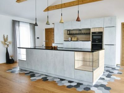 Moderne offene Küche mit zentraler Insel, individuellen Hängeleuchten und Holzelementen, gefertigt von Tischlerei Gangl.