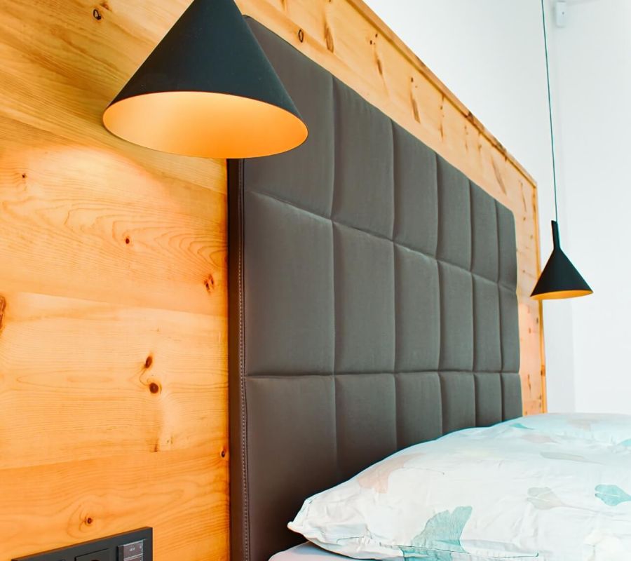 Gemütliches Schlafzimmer mit Holzwand und modernen Hängeleuchten, gefertigt von Tischlerei Gangl.