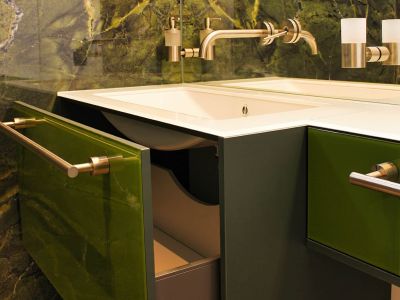 Elegantes Badezimmer mit grüner Schranktür und Natursteinwand, maßgeschneidert von Tischlerei Gangl.